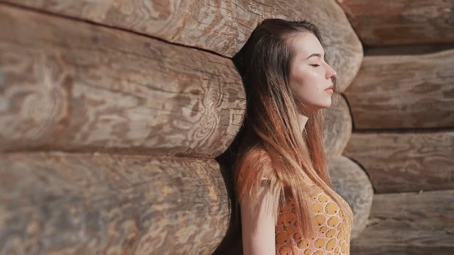 Beautiful sensual young girl with long hair and in a dress posing near a wooden wall from wide logs. Relaxation. Summer. The youth.