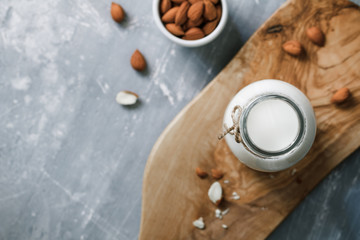 Top view of the almond milk in the glass bottle with almond nuts in the white bowl on the wooden decorative rustic cutting board.