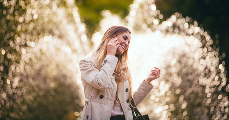 Fototapeta na wymiar Smiling woman wearing jacket walking in city and talking on smartphone