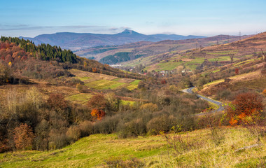 mountainous rural area in late autumn. trees with reddish foliage on green grassy hills. mountain ridge with high peak in the distance © Pellinni