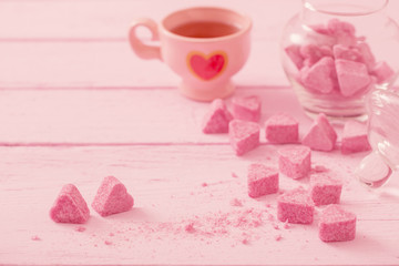 Granulated pink sugar  in the shape of heart and cup of tea  on a wooden background
