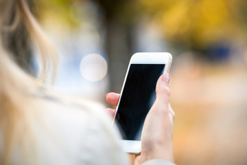 Closeup smartphone in hand with autumn street background