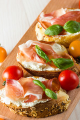 Italian tomato, prosciutto, jamon, ham and cheese bruschetta. Tapas, antipasti with chopped vegetables, herbs and oil on grilled ciabatta and baguette bread.