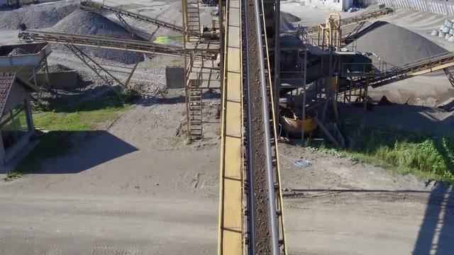 Aerial view, camera tracking conveyor belt that transporting rocks and soil while dropping on heap, stone crusher machine, mixer truck leaving, plant for sand and gravel production, building industry