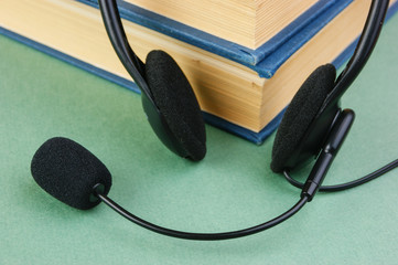 Headphones with a microphone and a stack of books on a green background
