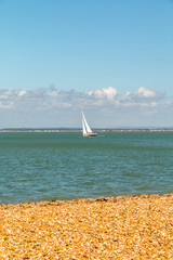 A yacht sails in the Solent off the pebble beach of Cowes on the Isle of Wight, England. The sailing capital of the world.