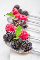 Fresh berries on steel spoons on white marble background  © Lsantilli