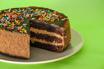 Chocolate cake with a colored powder and a cut piece on a light green background. Festive treats