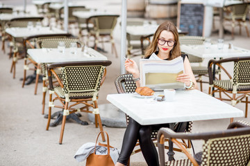 Young woman reading newspaper while sitting with cigarette during the breakfast outdoors at the typical french cafe terrace in France
