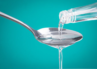 Coconut oil pouring from a bottle to spoon over green mint background
