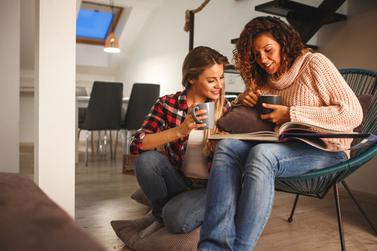 Two best female friends looking at family album.They sitting in living room and drinks coffee.