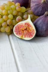 Fresh and ripe fig and grape fruits over white wooden board.