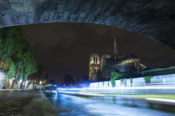 Notre-Dame de Paris by night. Famous ancient catholic cathedral on the quay of the Seine river and city lights reflection. Touristic historical and architectural landmark. Tourism and travel concept.