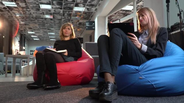 Two women in suits write something down in notepads and tablets and discussion with someone else