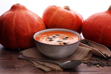 Roasted pumpkin and carrot soup with cream and pumpkin seeds on wooden background