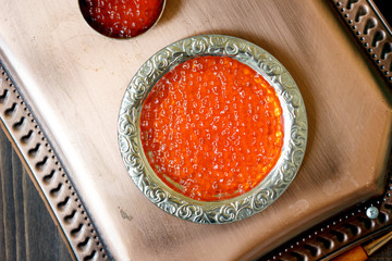 Top view of red caviar inside metal plate over copper tray.