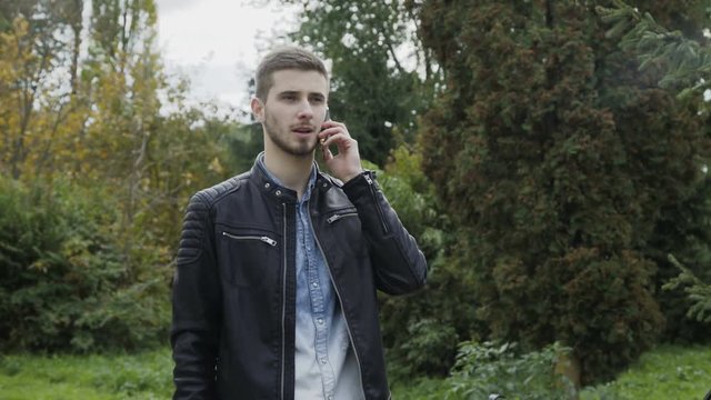 Young man speaking on a phone in a park 4K