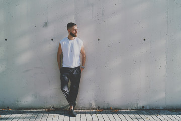 Bearded hipster guy wearing a blank white t-shirt is looking aside while standing on a light gray...