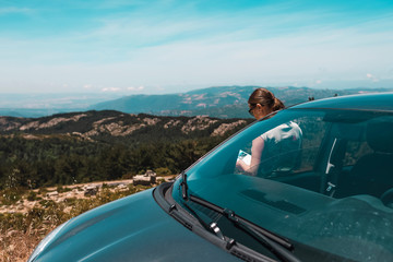 Woman leaning against car reading book in mountains. Sardinia. Italy.