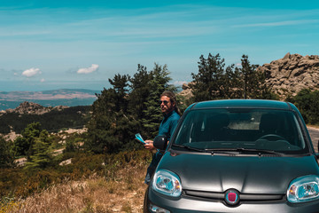 Fototapeta na wymiar Male tourist leaning against car parked in mountains. Sardinia. Italy.