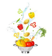 Different vegetables, water splashes and colander on white background