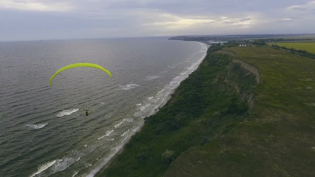 Paraplane, paraglider in the air aerial shot. Extreme man flies on a paraglider over a cliff near the sea. Extreme life.