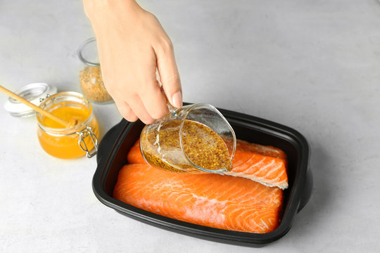 Woman preparing salmon fillet with honey mustard marinade in dish