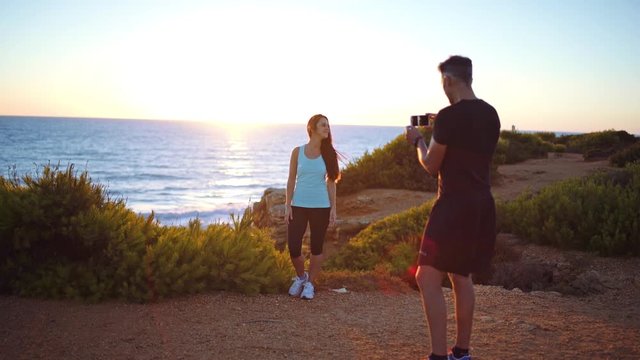 Loving couple enbraced together and taking photos in a beautiful place. Couple wearing sports near to the sea at sunset