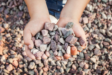Child holding small colorful stones in little hands. Concept of game money, valuable resource