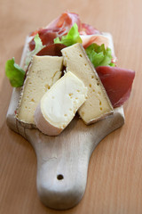 A wooden cutting board with french cheese and prosciutto
