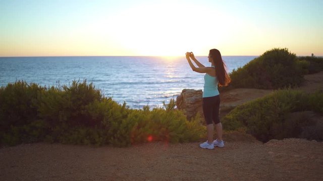 Running woman watch the sea and takes a photo in a beautiful place at sunset