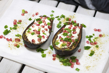 Grilled and baked eggplants with cream sauce, pomegranate and chive. Wooden white background