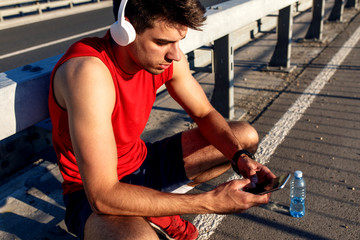 Portrait of young athlete man using mobile phone on bridge.