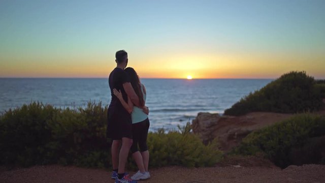 Loving couple enbraced together and taking photos in a beautiful place. Couple wearing sports near to the sea at sunset