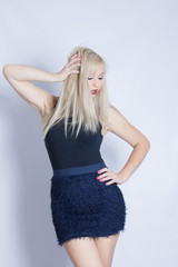 Fototapeta premium Portrait of a beautiful young blond woman in studio on a white background. Girl posing in blue skirt and black blouse.