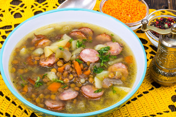 Soup with lentils, celery and sausages on old wooden table