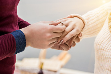 Pleasant moment of engagement. Cropped image of man putting on engagement ring on his wife finger while standing outdoors. Marriage proposal concept. Man and woman engaged. Romance of couple in love.