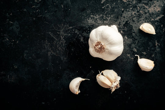 Raw garlic cloves and bulb on antique dark black background. Top view with copy space.