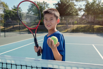 Young tween multiethnic Asian boy tennis player on outdoor blue court