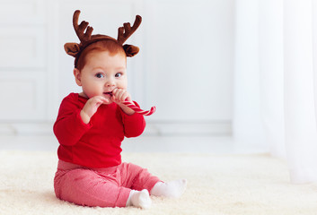 cute little redhead baby boy with reindeer band tasting christmas sweet treats, sitting on the floor at home