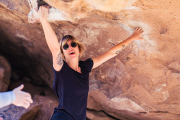Thin blonde caucasian woman with arm tattoos rock climbs on boulders in the desert of California
