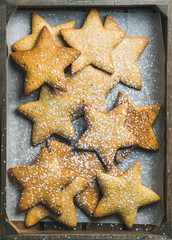 Sweet Christmas holiday gingerbread cookies in shape of stars with sugar powder on baking paper in rustic wooden tray, top view, vertical composition