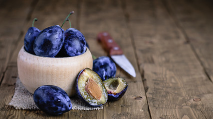 Beautiful blue plum in a wooden bowl with a knife on a vintage table.