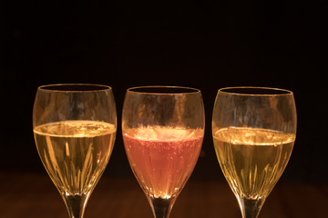 Three Wine Glasses against a black background with golden and pink colored beverages inside the glasses