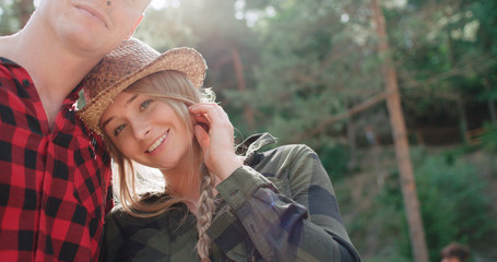 Portrait of beautiful caucasian couple spending time in a forest during sunny day. Smiling couple looking at camera while relaxing in woods.