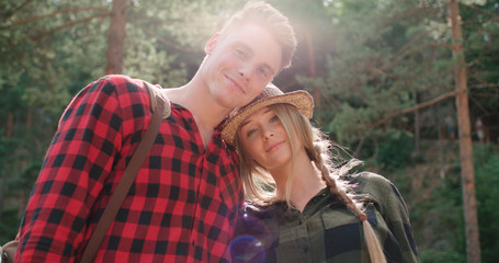 Portrait of beautiful caucasian couple spending time in a forest during sunny day. Smiling couple looking at camera while relaxing in woods.