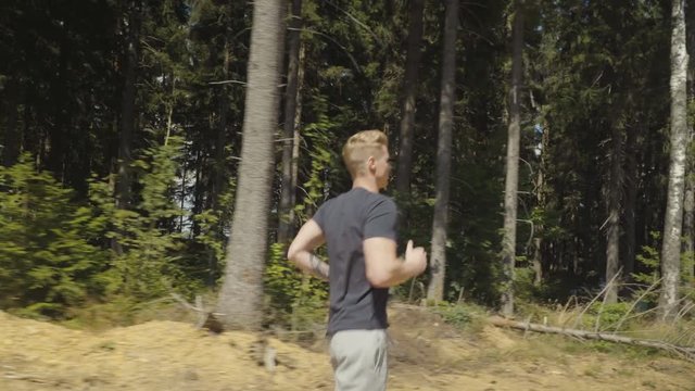 Handsome caucasian man running in a forest during sunny day. 