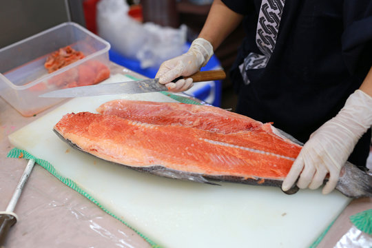 Japanese chef slicing raw fish for salmon sushi. Chef preparing a fresh salmon on a cutting board.
