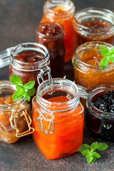Various jars of fruit jam on dark table. Selective focus