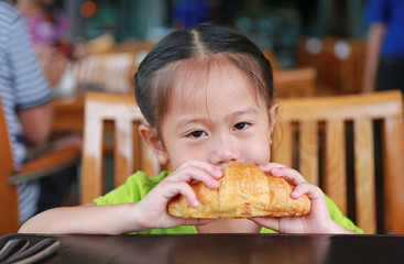 Cute little girl eating croissant at restaurant.